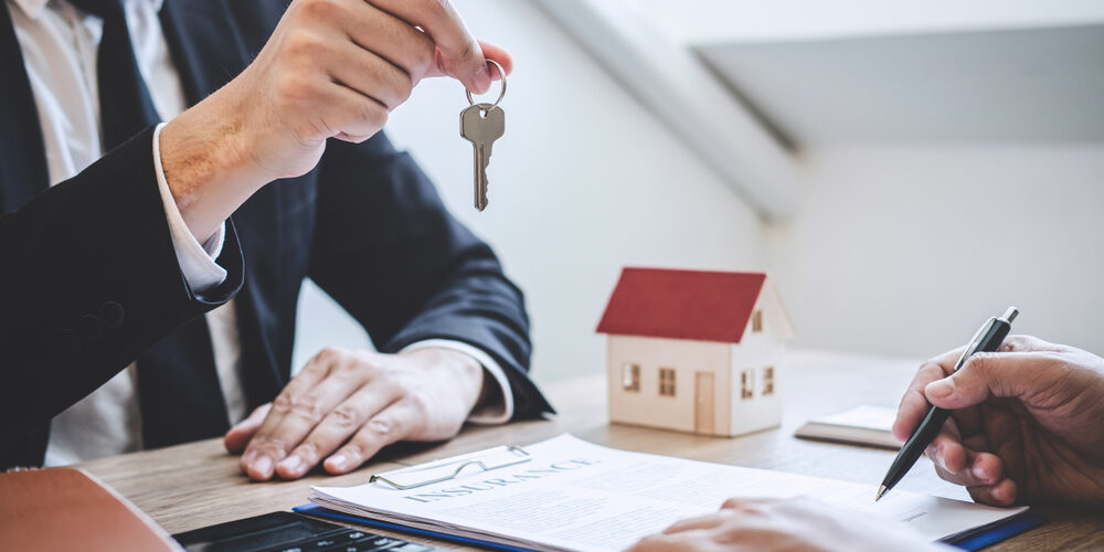 Seller handing over keys. A model house sits in the background.